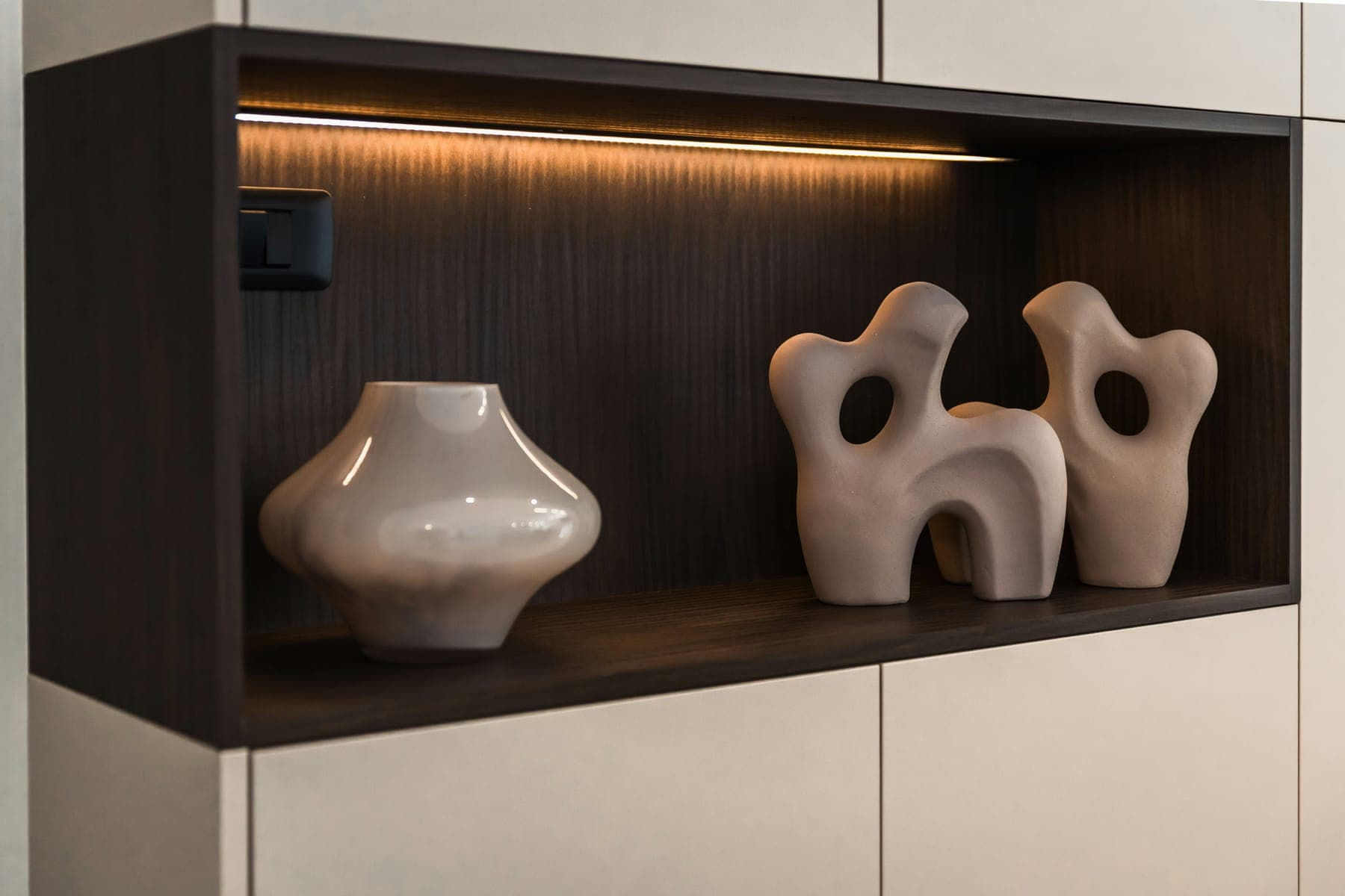 Warm LED strip lighting a dark wood display niche with sculptures