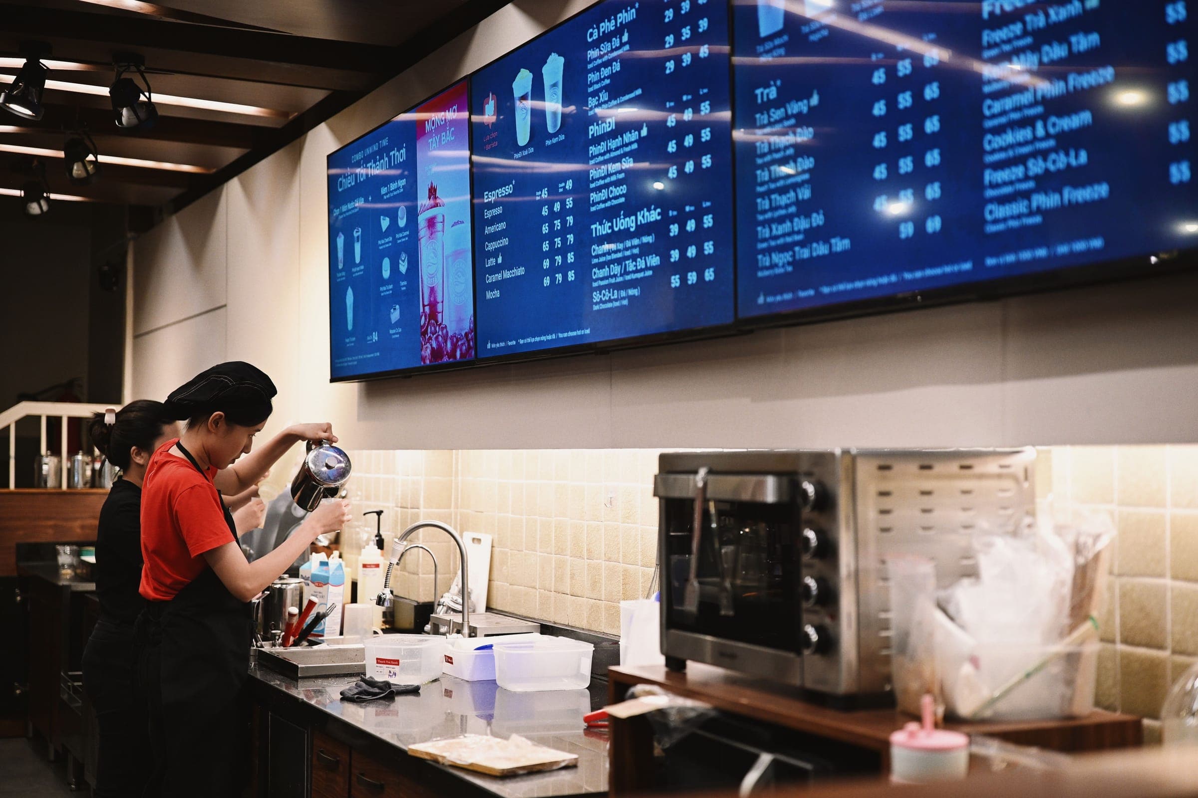 Digital menu boards above a café counter with baristas at work