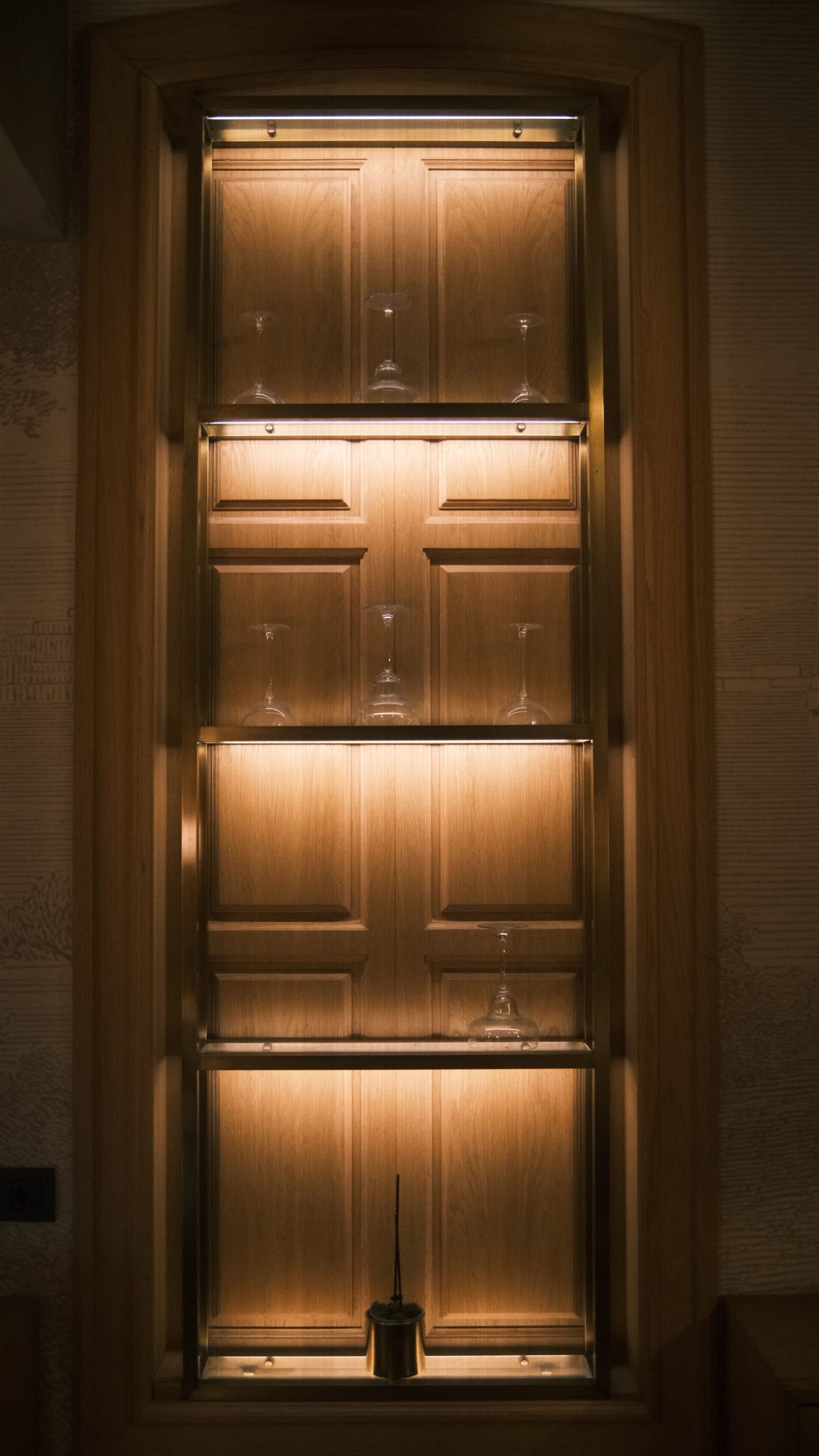 Dark glass-front cabinet with warm lit shelves holding glassware